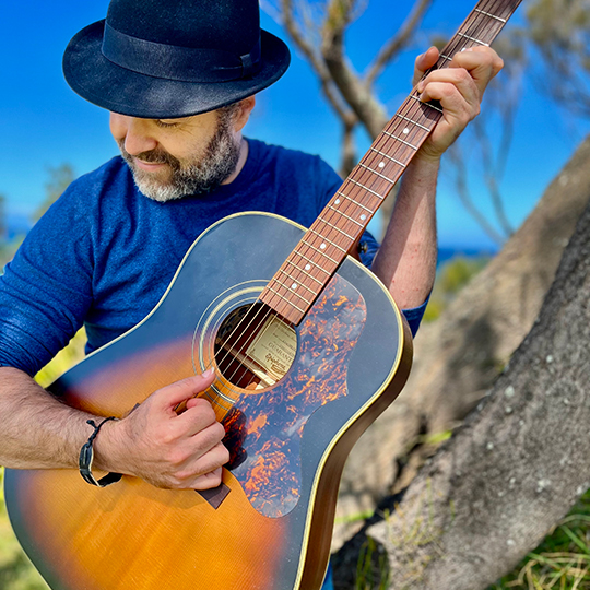 A man in a blue shirt and hat playing the guitar